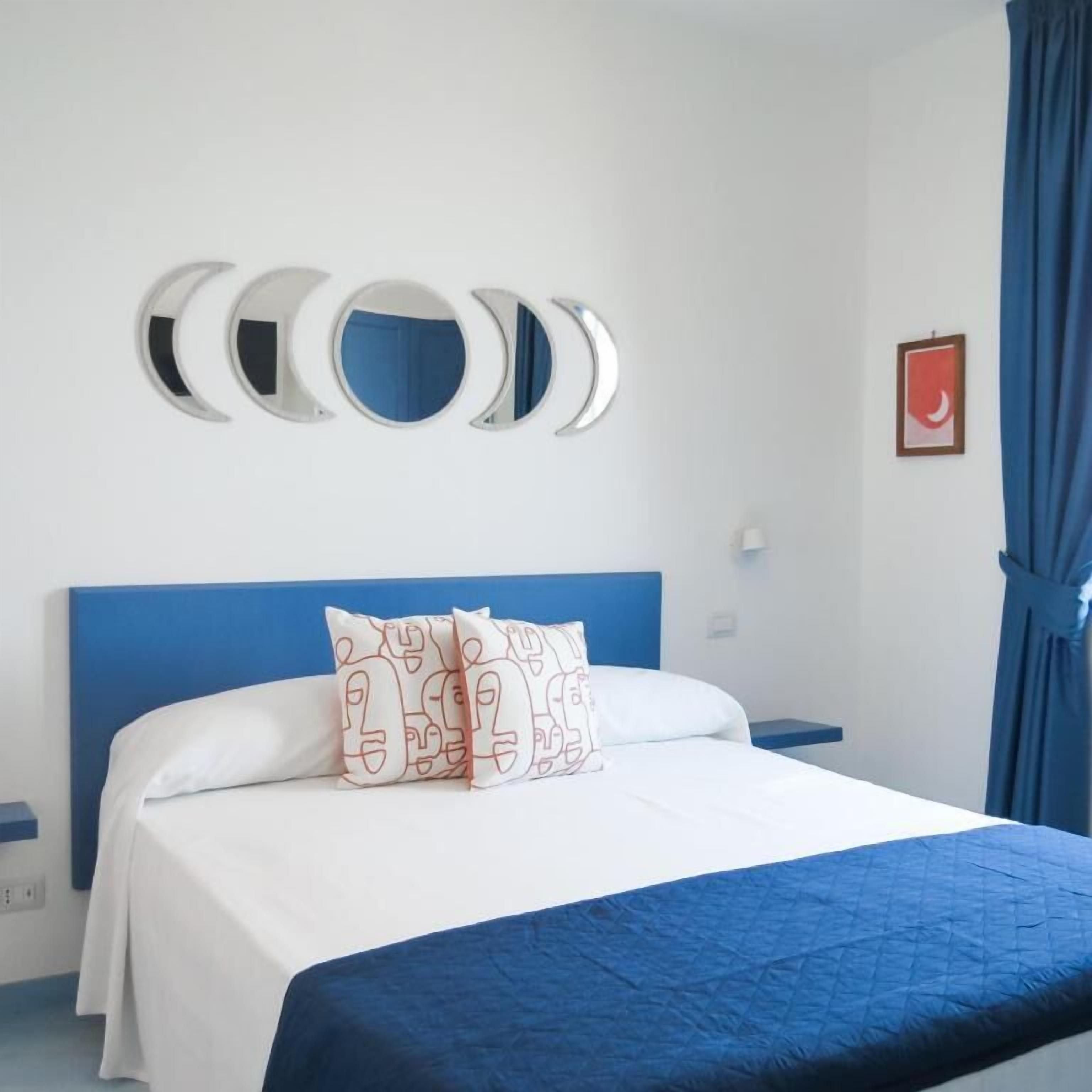 A bedroom with a blue headboard, white bedding, and decorative wall mirrors.