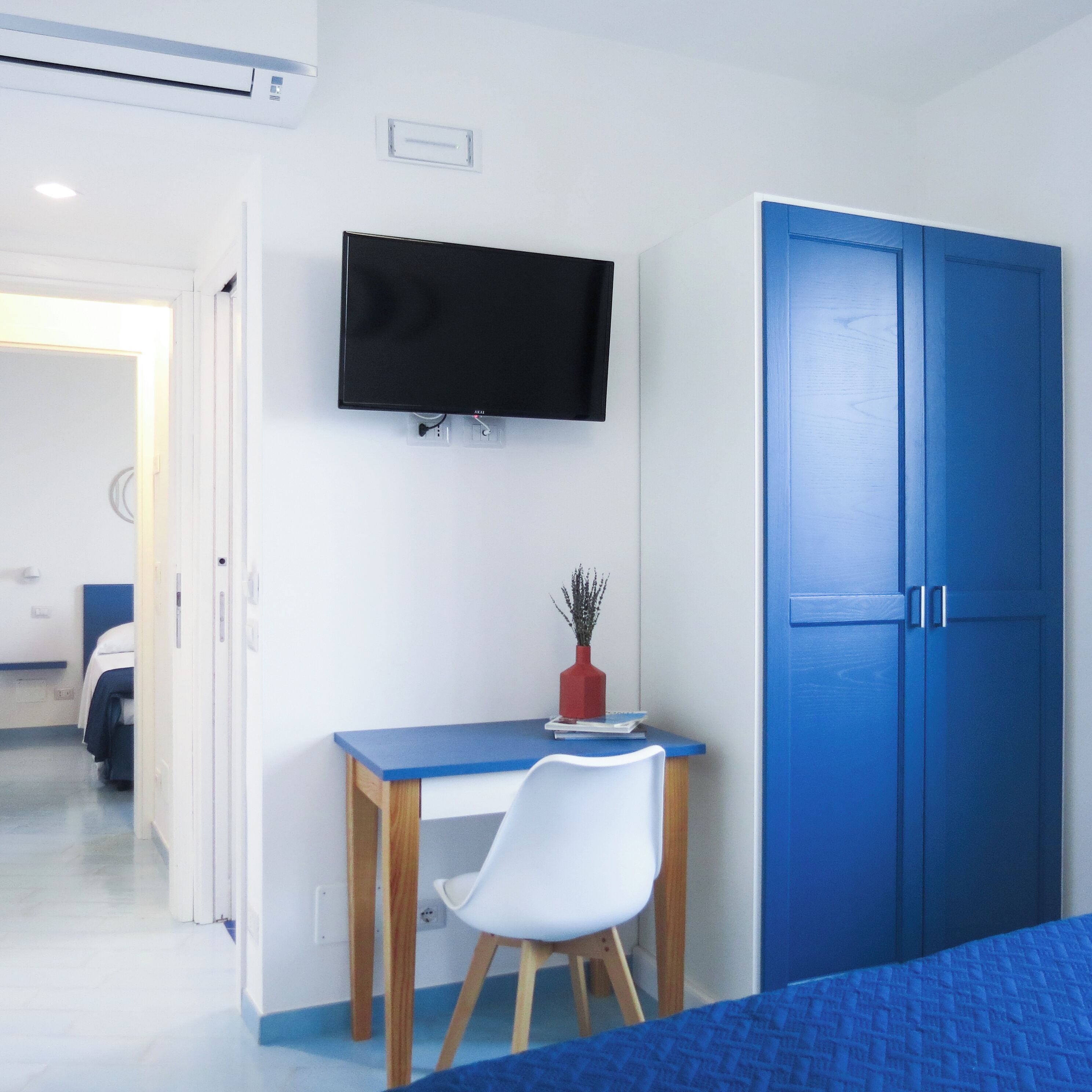 Un dormitorio con una cama, un escritorio con una silla, un televisor montado en la pared y un armario.