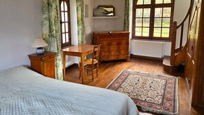 Een slaapkamer met een bed, een houten bureau, een stoel, een dressoir en een groot raam.