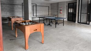 A modern indoor space with a foosball table, a ping pong table, and a foosball table in the background.