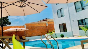 A pool area with multiple umbrellas, a pool, and a building with large windows. - 2-bedroom apartment in Kigali with AC, a swimming pool, and great city views. (Kigali)