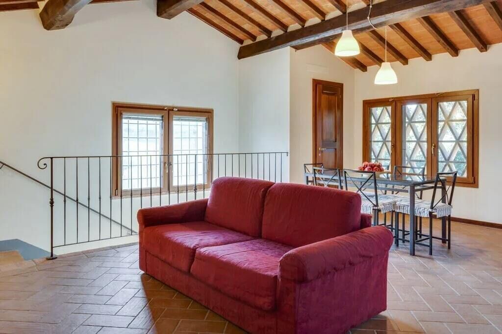Une pièce spacieuse avec un canapé rouge, une table à manger et des chaises, ainsi qu’un escalier doté d’une rampe en métal.