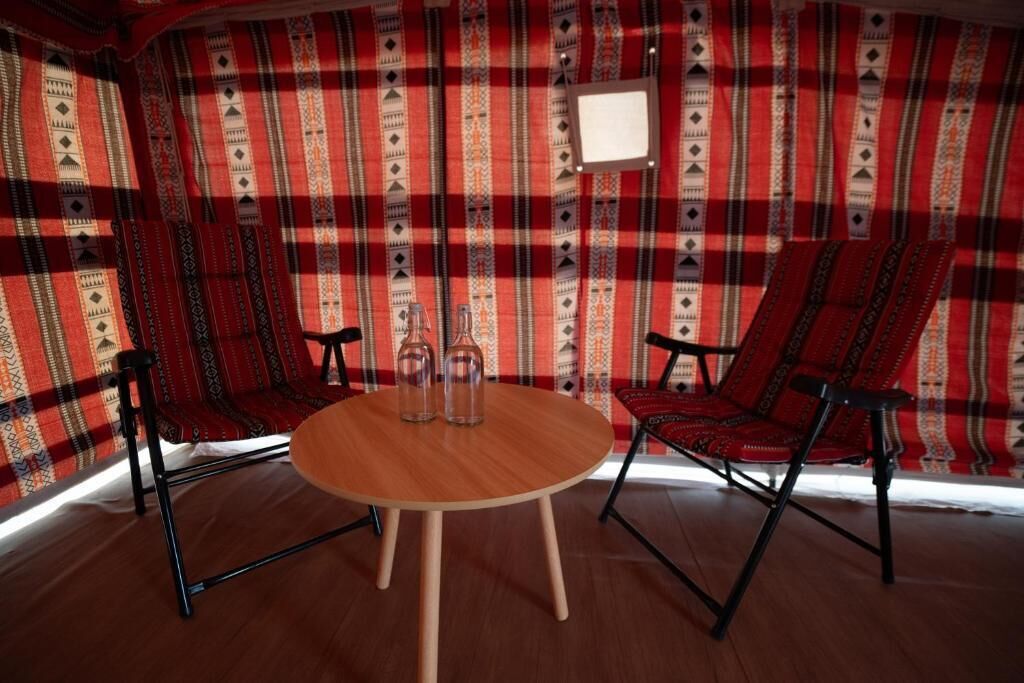 Une pièce avec une table ronde en bois, deux chaises noires et un mur décoré d’un motif rouge et blanc.