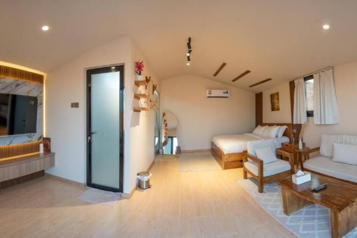 A modern living room with a flat-screen TV, a sofa set, a wooden coffee table, and a bed with a white duvet.