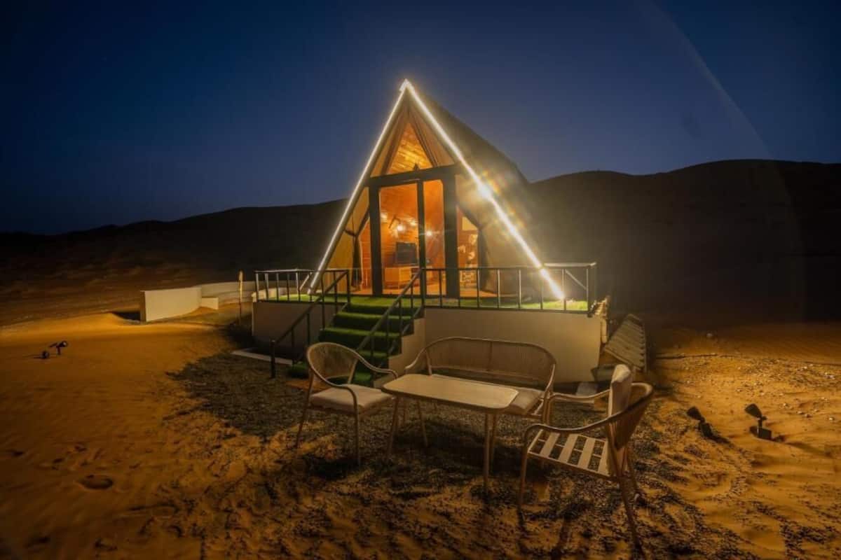 A desert lodge with a triangular roof, a staircase leading to the entrance, and outdoor seating.