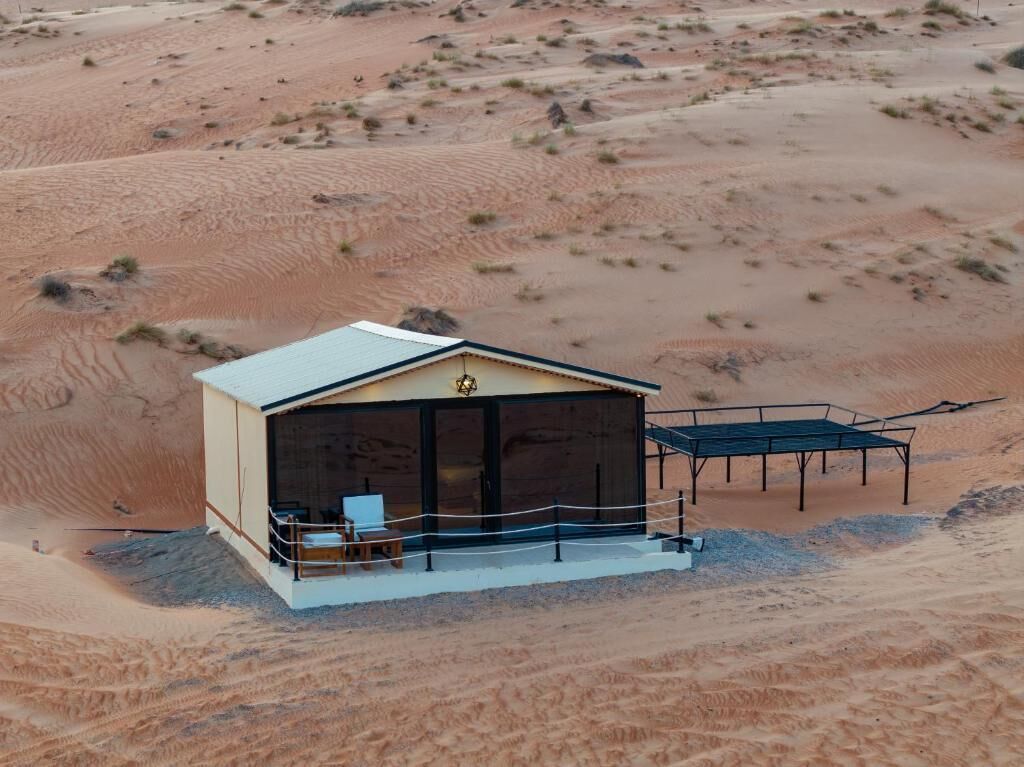 A desert lodge with a flat roof, a covered outdoor seating area, and a view of the surrounding dunes.