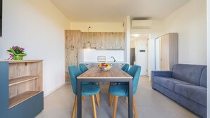 Una sala de estar moderna con una mesa de comedor de madera, sillas azules, un sofá gris y una cocina al fondo.