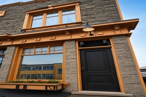 A building with a stone facade, large windows, a black door, and a small outdoor planter.