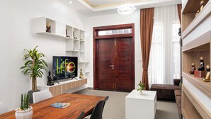 A modern living room with a wooden dining table, white shelves, a TV, and a large wooden door. - 2 Bedrm Villa+ Living Room, 15 mins walk to Center (Krong Siem Reap)