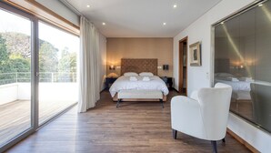 Een moderne slaapkamer met een groot bed, een zithoek en een balkon met uitzicht op bomen.