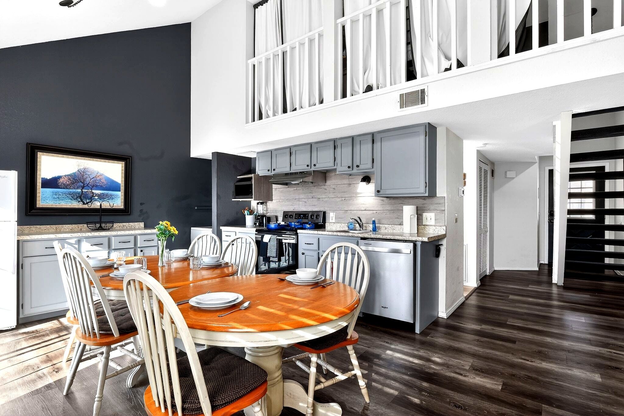 A modern kitchen with a dining area, a TV mounted on the wall, and a staircase leading to an upper level.