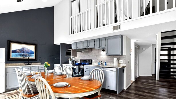 A modern kitchen with a dining area, a TV mounted on the wall, and a staircase leading to an upper level. - Lake Views•Near SDC•Game Nights•2 Decks•King Bed•Marina Access•Resort Amenities! (Branson)