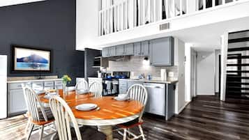 A modern kitchen with a dining area, a TV mounted on the wall, and a staircase leading to an upper level.