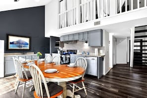 Una cocina moderna con comedor, un televisor montado en la pared y una escalera que sube a un nivel superior.