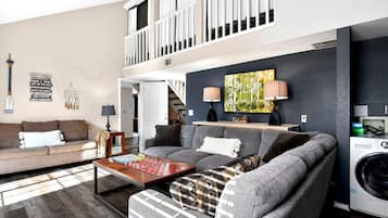 A living room with a sofa, a coffee table, a washing machine, and a painting on the wall.