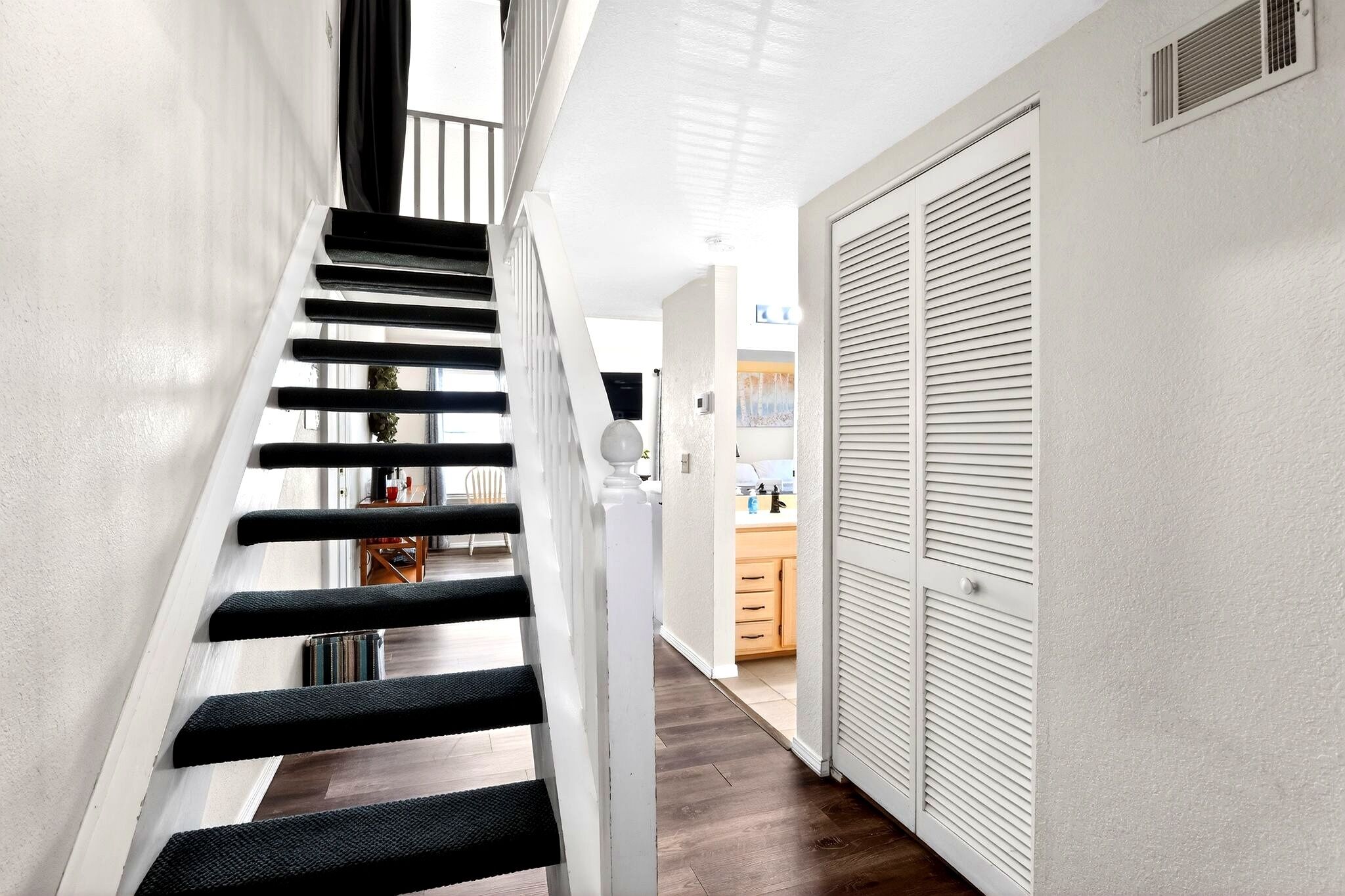 A staircase with black steps and white walls, leading to a kitchen area with wooden cabinets and a countertop.