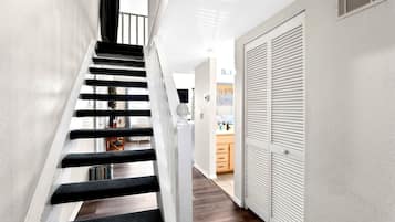 A staircase with black steps and white walls, leading to a kitchen area with wooden cabinets and a countertop.