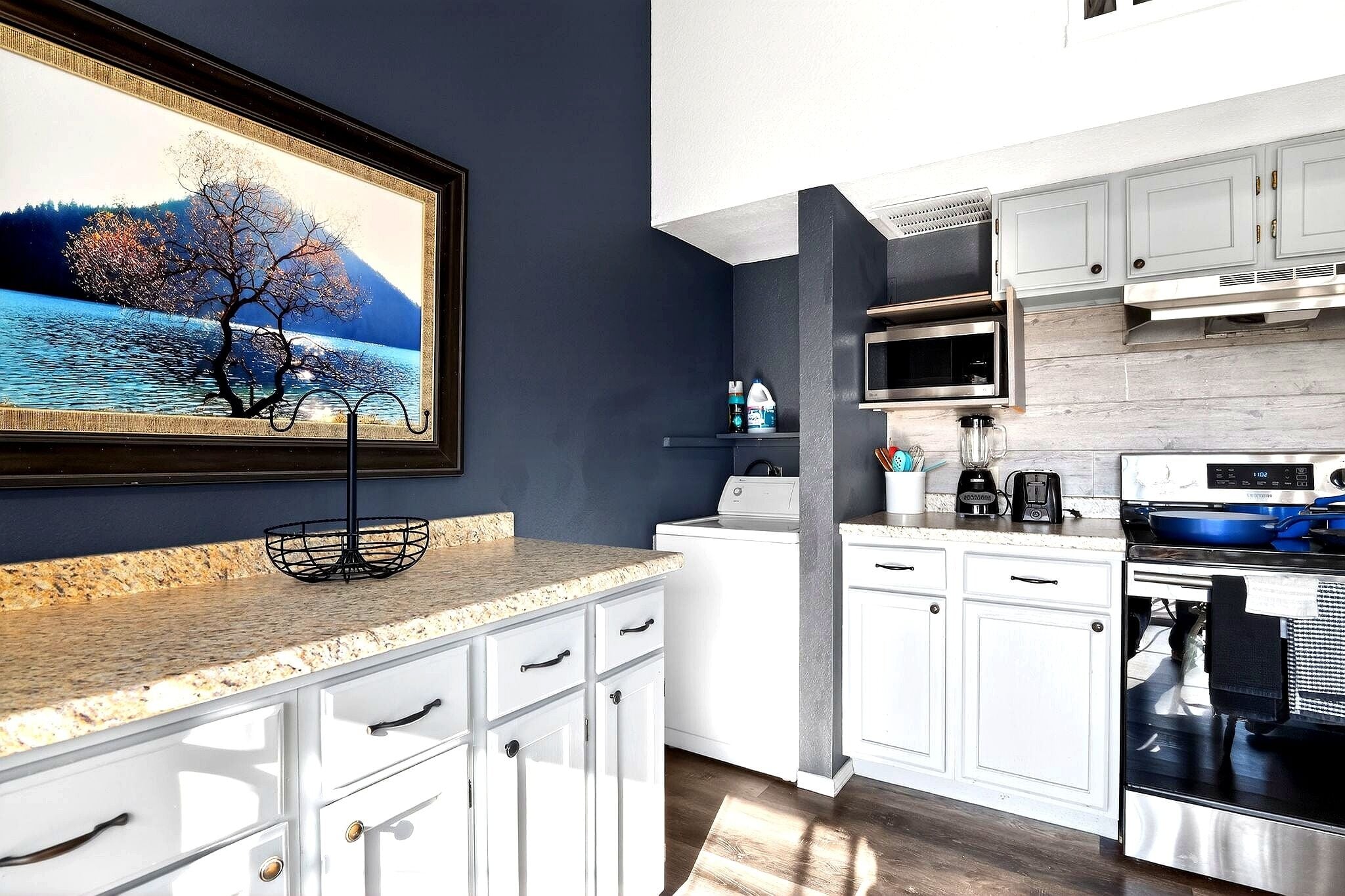 A modern kitchen with white cabinets, a granite countertop, a stainless steel oven, and a microwave.