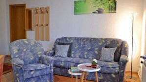 Un soggiorno con divano e poltrona, un tavolino con una pianta e un quadro appeso al muro.