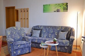 Ein Wohnzimmer mit einer Couch und einem Sessel, einem kleinen Tisch mit einer Pflanze und einem Bild an der Wand.