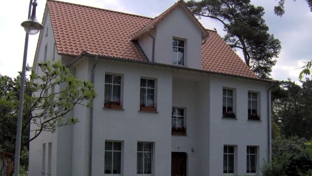 Un edificio a due piani con tetto in tegole rosse, diverse finestre e un piccolo portico.