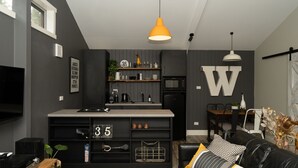 A modern kitchen with a built-in oven, a dining area with a black leather couch, and a large white 'W' on the wall. - The Duckling quintessential bush retreat set amongst towering gums. One bedroom - dog friendly (Wheatsheaf)