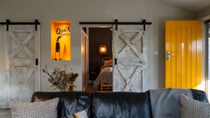A living room with a black leather sofa, a yellow door, and a bed with checkered bedding. - The Duckling quintessential bush retreat set amongst towering gums. One bedroom - dog friendly (Wheatsheaf)