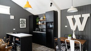 Une cuisine compacte dotée d’un îlot central, d’un coin repas avec une table en bois et d’une grande décoration en forme de « W » sur le mur.