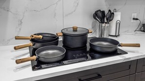 A kitchen with a white marble countertop, a black induction cooktop, and various pots and pans with wooden handles. - Kayaks/LocatedonCanal/Sunsets/HeatedPool (Hernando Beach)