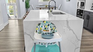 A modern kitchen with a marble island, a built-in sink, and a high chair. - Kayaks/LocatedonCanal/Sunsets/HeatedPool (Hernando Beach)