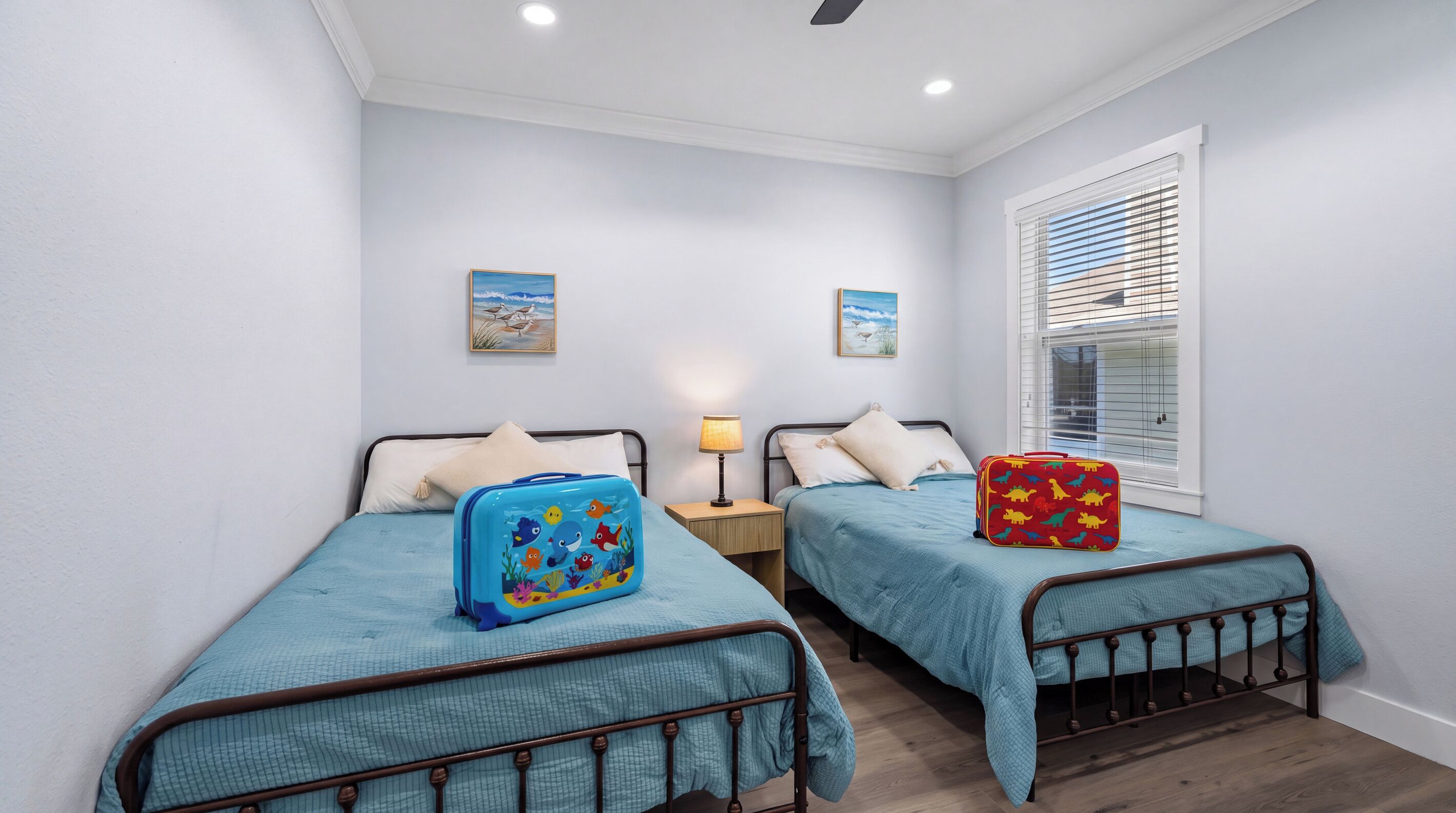 A bedroom with two beds, a window with blinds, and a nightstand with a lamp.