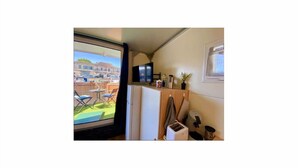 A compact kitchen with a window overlooking a courtyard, a small refrigerator, and a flat-screen TV mounted on the wall.