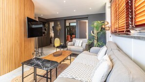Een moderne woonkamer met een flatscreen-tv, een houten accentmuur, een bank, een salontafel en een eethoek.