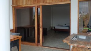 Une pièce comprenant un meuble en bois, une porte-fenêtre coulissante donnant sur un balcon, un lit et un petit coin cuisine avec un évier.
