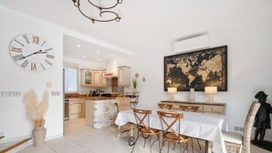 Una cocina moderna con armarios blancos, un reloj grande y una zona de comedor con mesa y sillas.