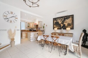 A modern kitchen with white cabinets, a large clock, and a dining area with a table and chairs. - Villa les Citronniers - Piscine, 100 m de la plage (Sainte-Maxime)