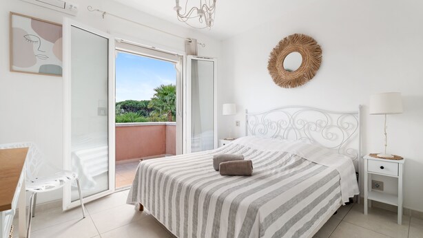 Un dormitorio con cama, mesita de noche, una silla y vistas al exterior.
