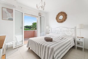 A bedroom with a bed, a nightstand, a chair, and a view of the outdoors. - Villa les Citronniers - Piscine, 100 m de la plage (Sainte-Maxime)