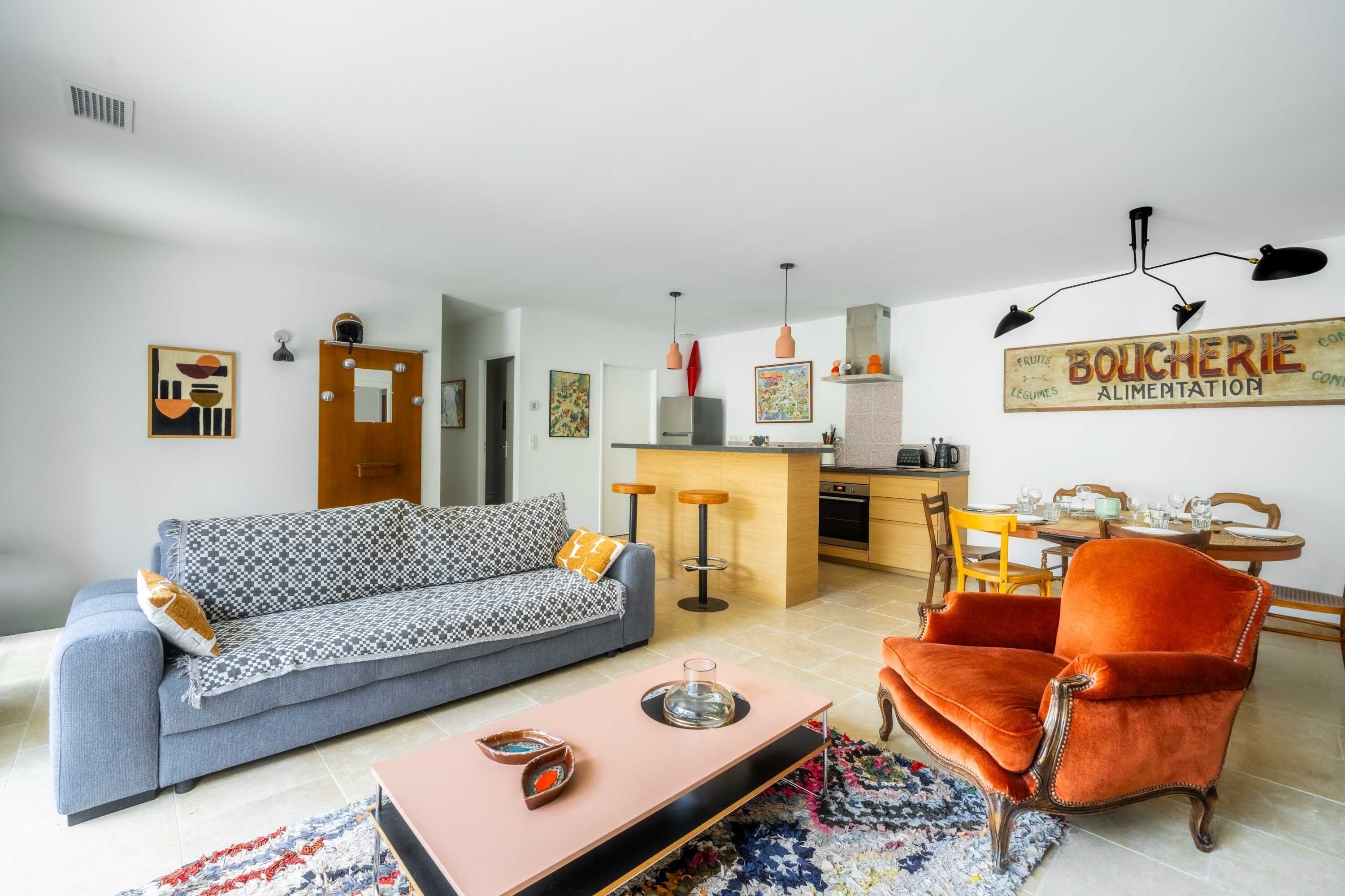Un salon comprenant un canapé, une table basse et un fauteuil orange vif. Il y a également un coin cuisine avec une table à manger et des chaises.