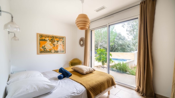 A bedroom with a bed, a window with curtains, a hanging light fixture, and a poster on the wall. - Maison Jeannot - Climatisée avec piscine (Vers-Pont-du-Gard)