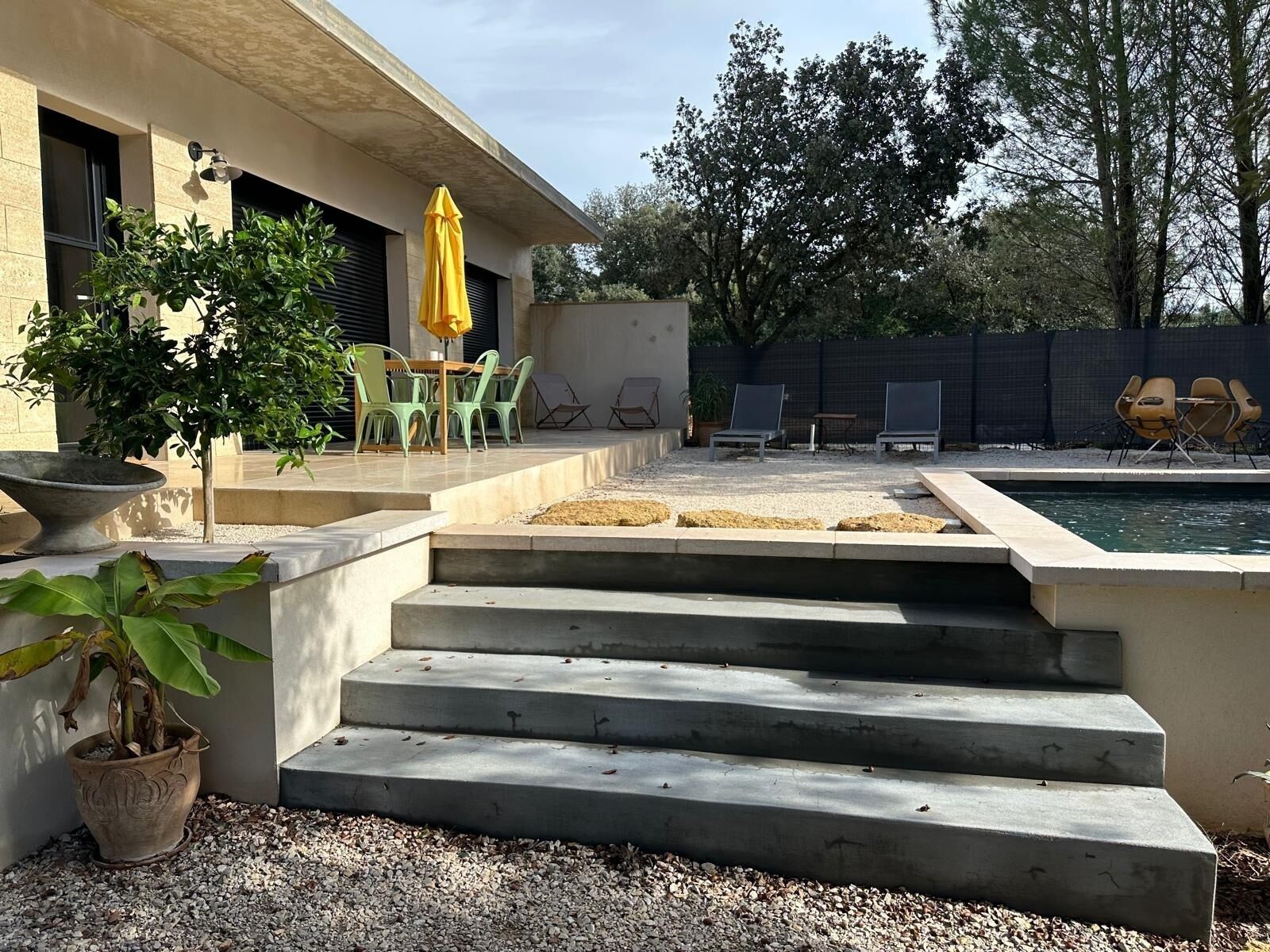 Un espace patio avec une piscine, des sièges d’extérieur et des marches menant à une zone aménagée au bord de la piscine.