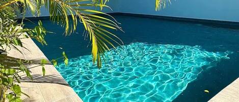 Une piscine d’un bleu éclatant, entourée d’un sol carrelé et de palmiers.