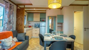 Une cuisine moderne avec des poutres en bois, un coin repas avec une table dressée pour quatre personnes, et un salon confortable avec un canapé et des coussins.
