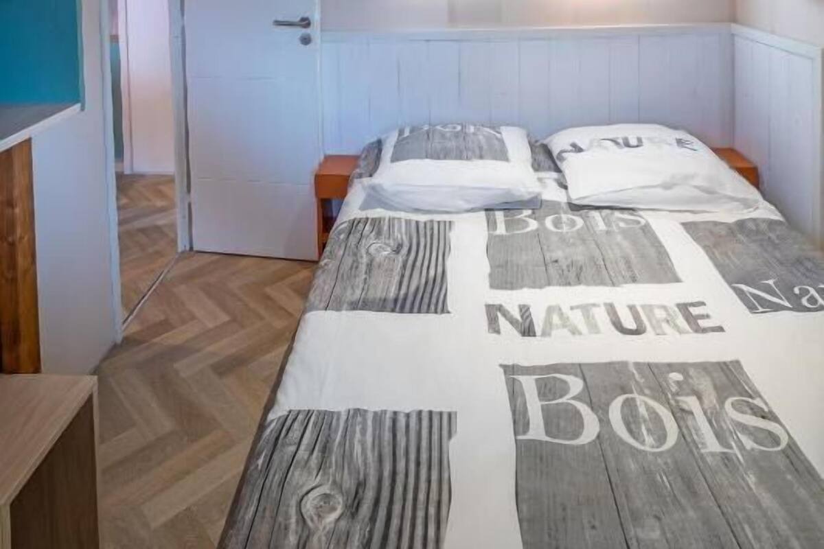 Ein Schlafzimmer mit einem Bett, Holzbalken, einer weißen Tür und einem Regal mit bunten Bauklötzen.