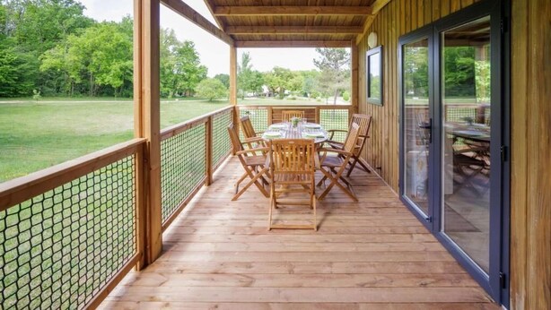 Un espace extérieur abrité, doté d’une terrasse en bois, d’une table avec des chaises et offrant une vue sur un champ verdoyant.