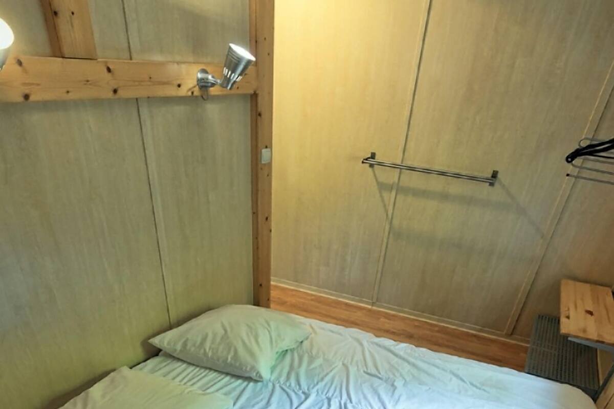 Ein Bett mit weißer Bettwäsche in einem Zimmer mit Holzwänden und einer Metallstange an der Wand.