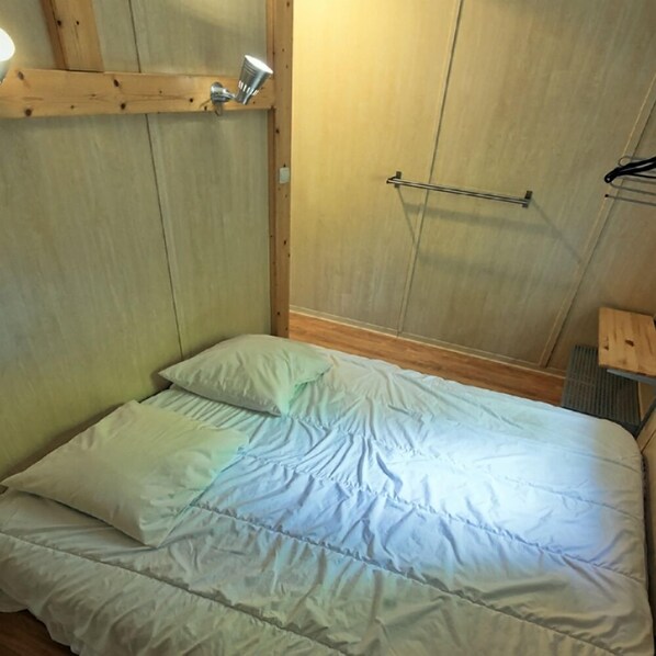 Una cama con ropa de cama blanca en una habitación con paredes de madera y una barra de metal en la pared.