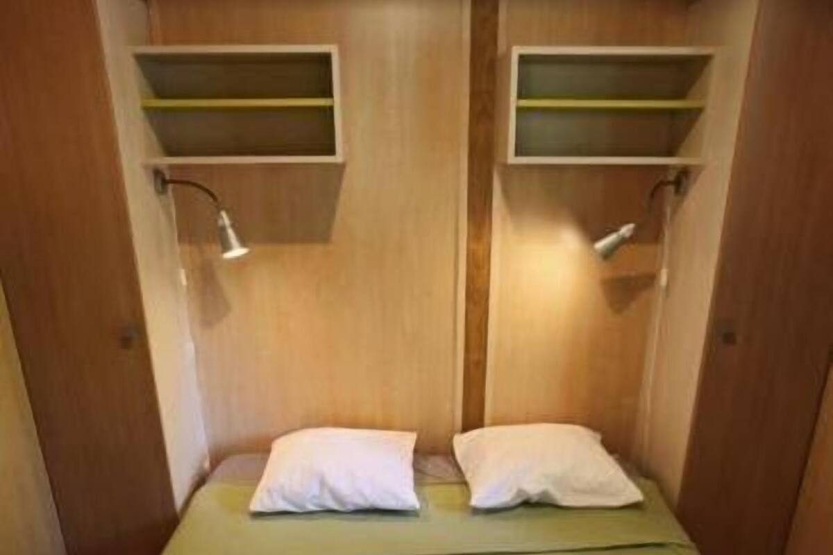 Ein kleines Zimmer mit einem Einzelbett, einem Holzkopfteil, zwei Nachttischen mit Lampen und einer grünen Bettdecke.