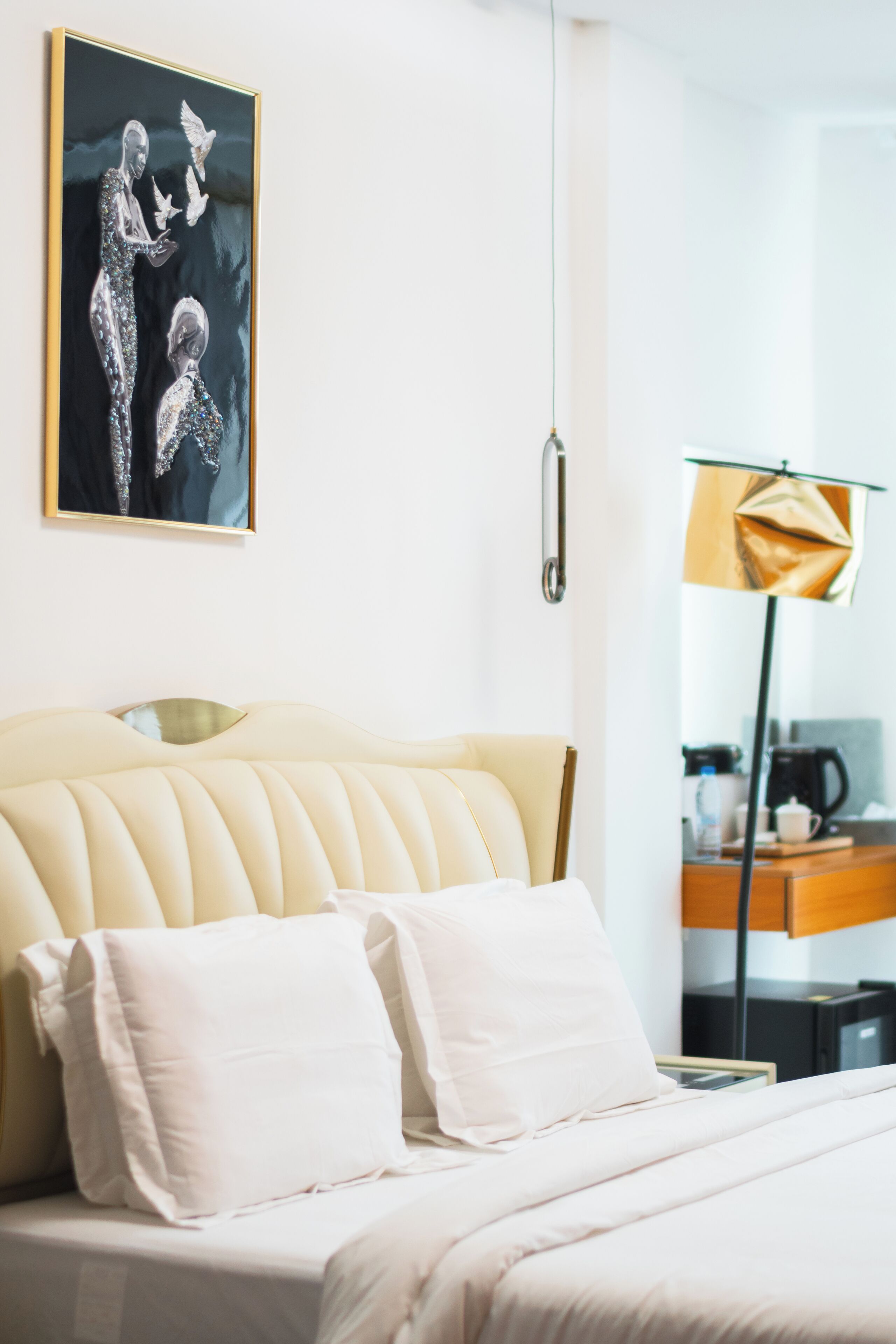 Ein modernes Hotelzimmer mit einem großen Bett, einem Bild an der Wand, einer Lampe und einer Kaffeemaschine auf dem Nachttisch.