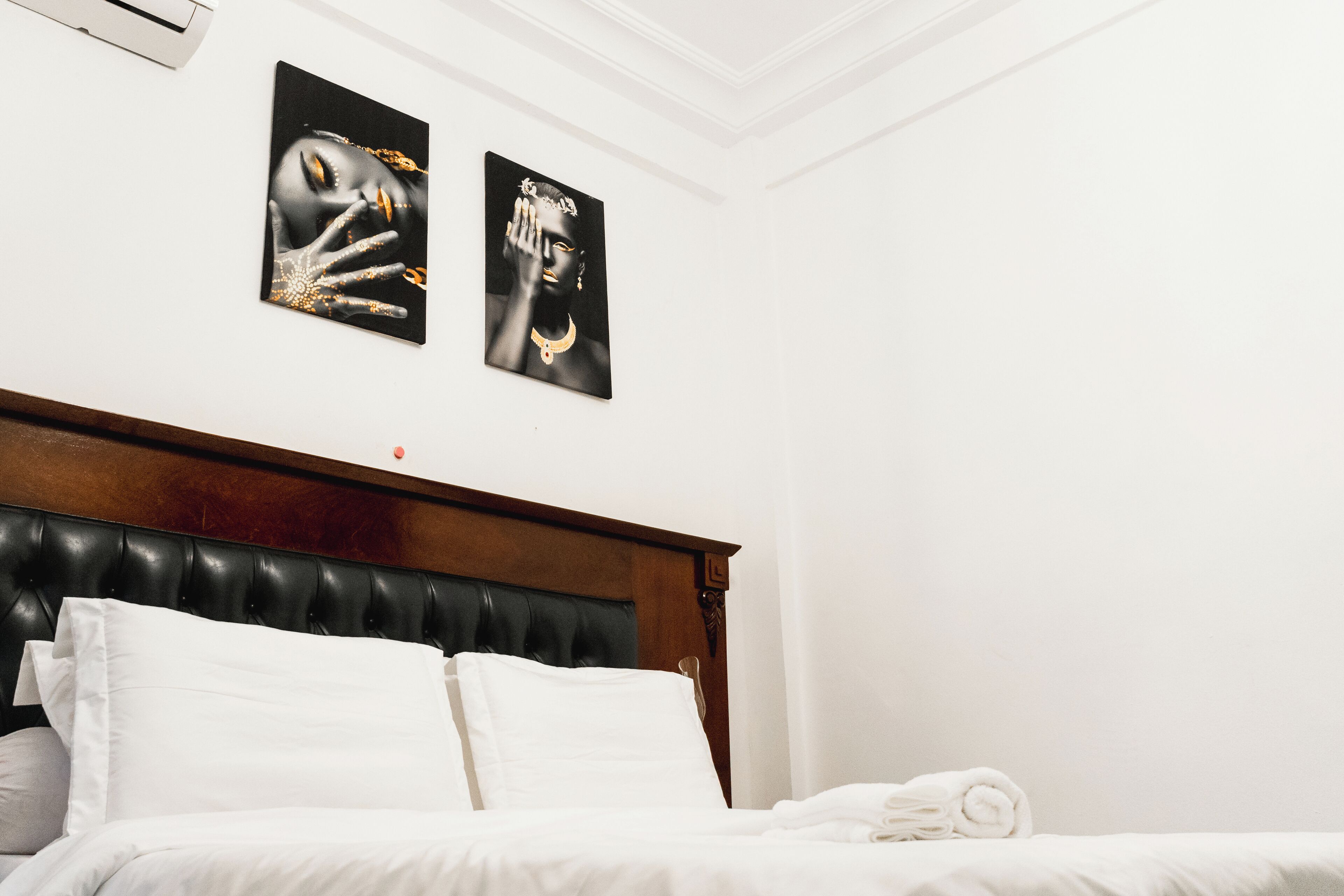 A hotel room with a wooden headboard, white bedding, and two black-and-white artwork pieces on the wall.